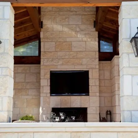 Outdoor TV installation above fireplace on stone wall.