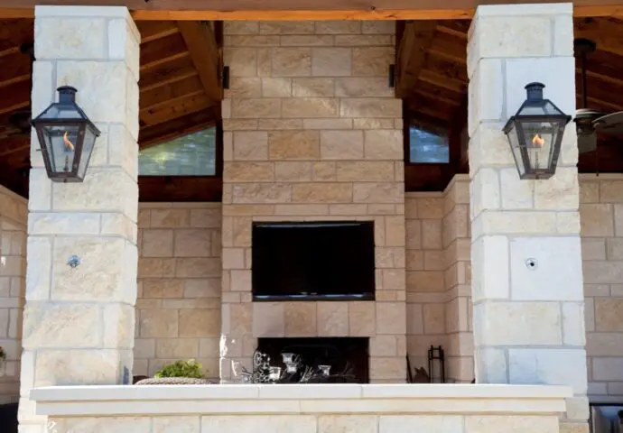 Outdoor TV installation above fireplace on stone wall.