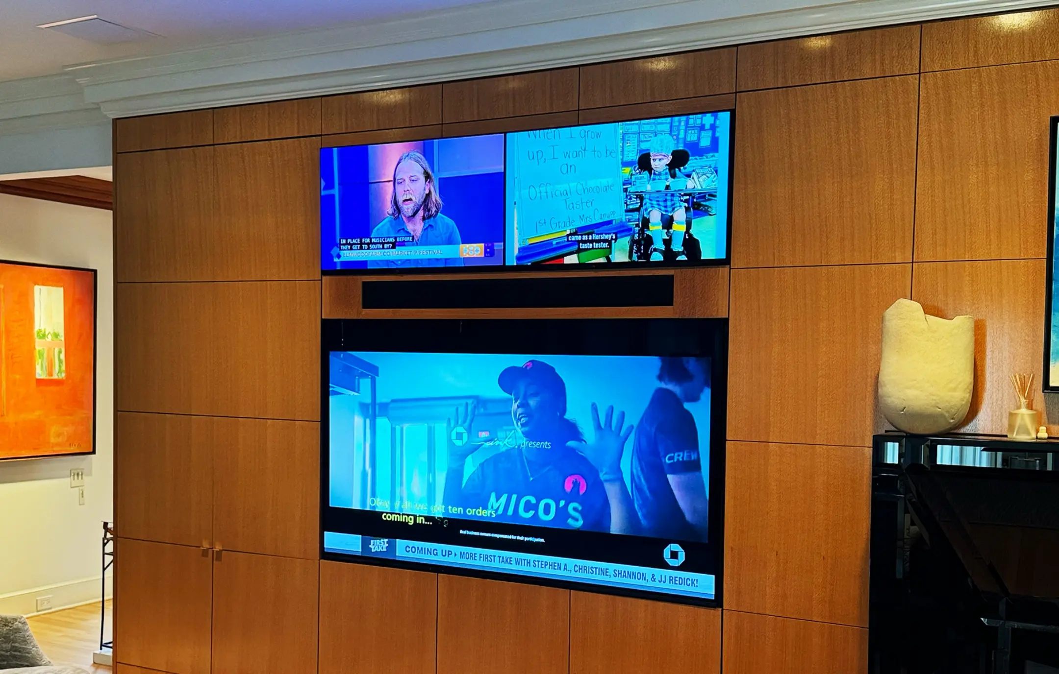 Three screen television installation with sound bar over wood paneled wall.