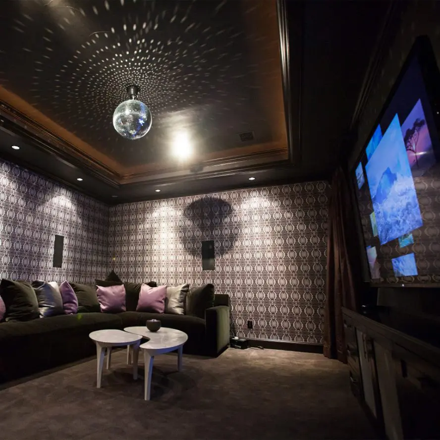 High-end home theater with AV installation, wallpapered walls, sofa, surround sound and disco ball lighting.