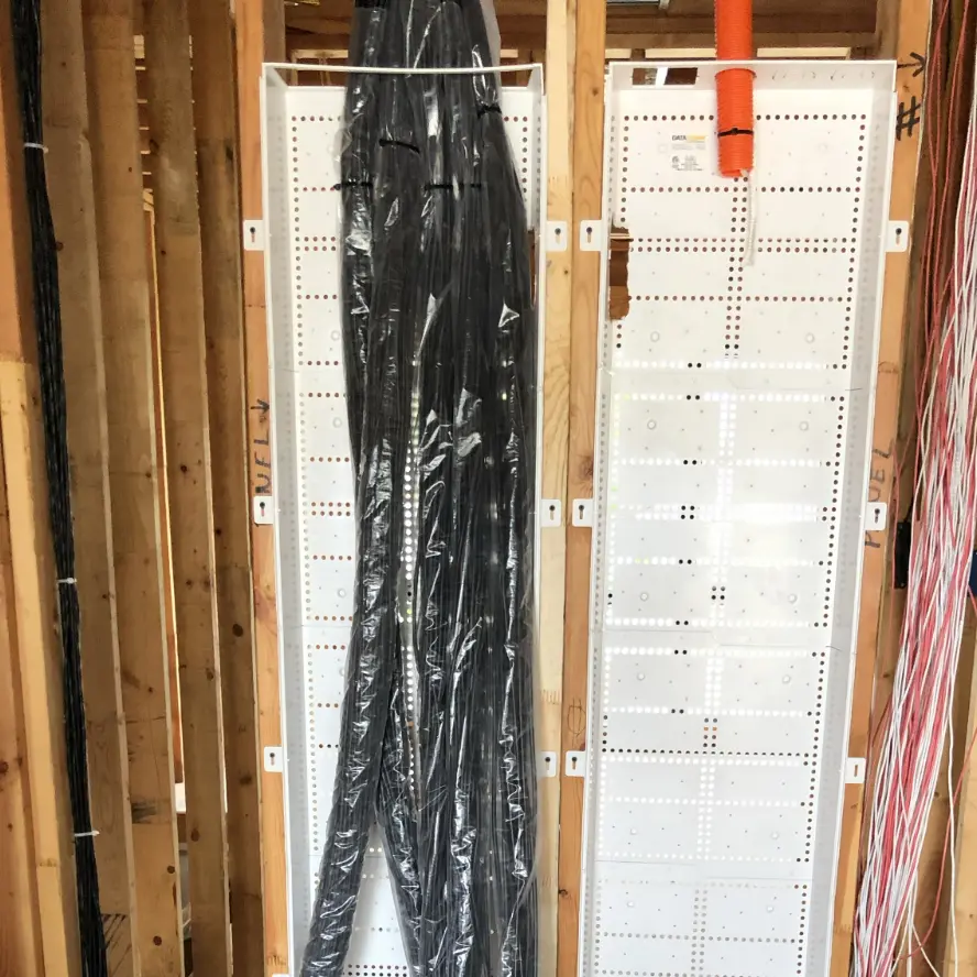 Professional cabling in new home construction wall with plastic tubing and labels.